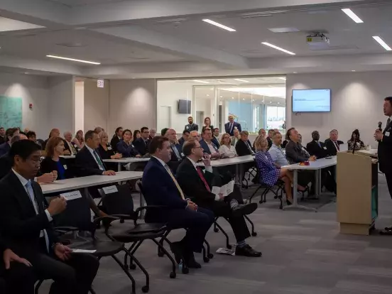 Photo of a large lecture room filled with people while Dr. Nakao stands at the podium giving a speech