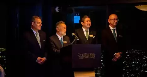 Scott Bradshaw, Kiyotaka Nakao, and Torsten Gilles gathered next to a podium where Makoto Nakao is speaking 